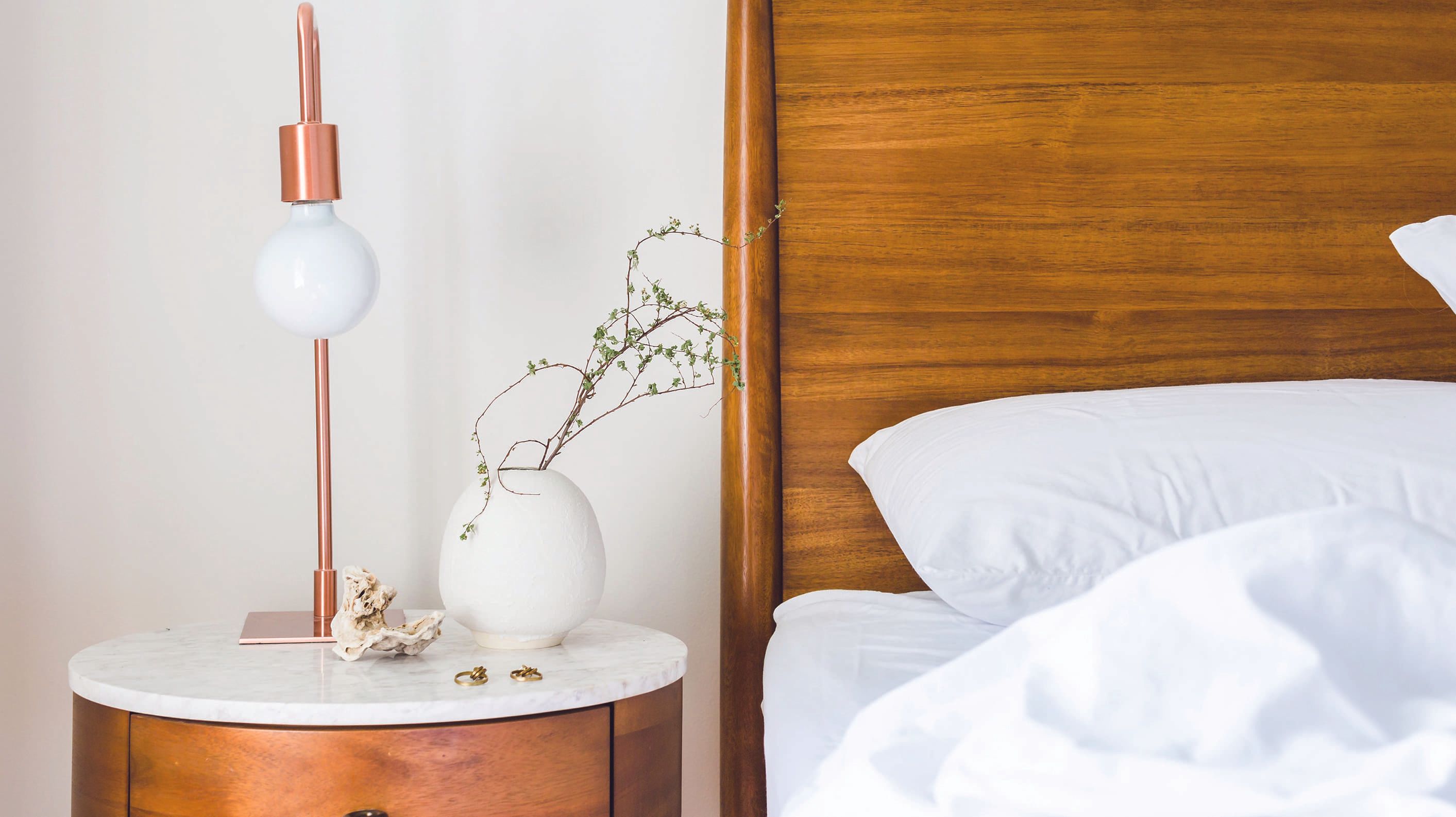 Cozy bedroom corner with a wooden bed, lamp, and minimalist decor on a nightstand.