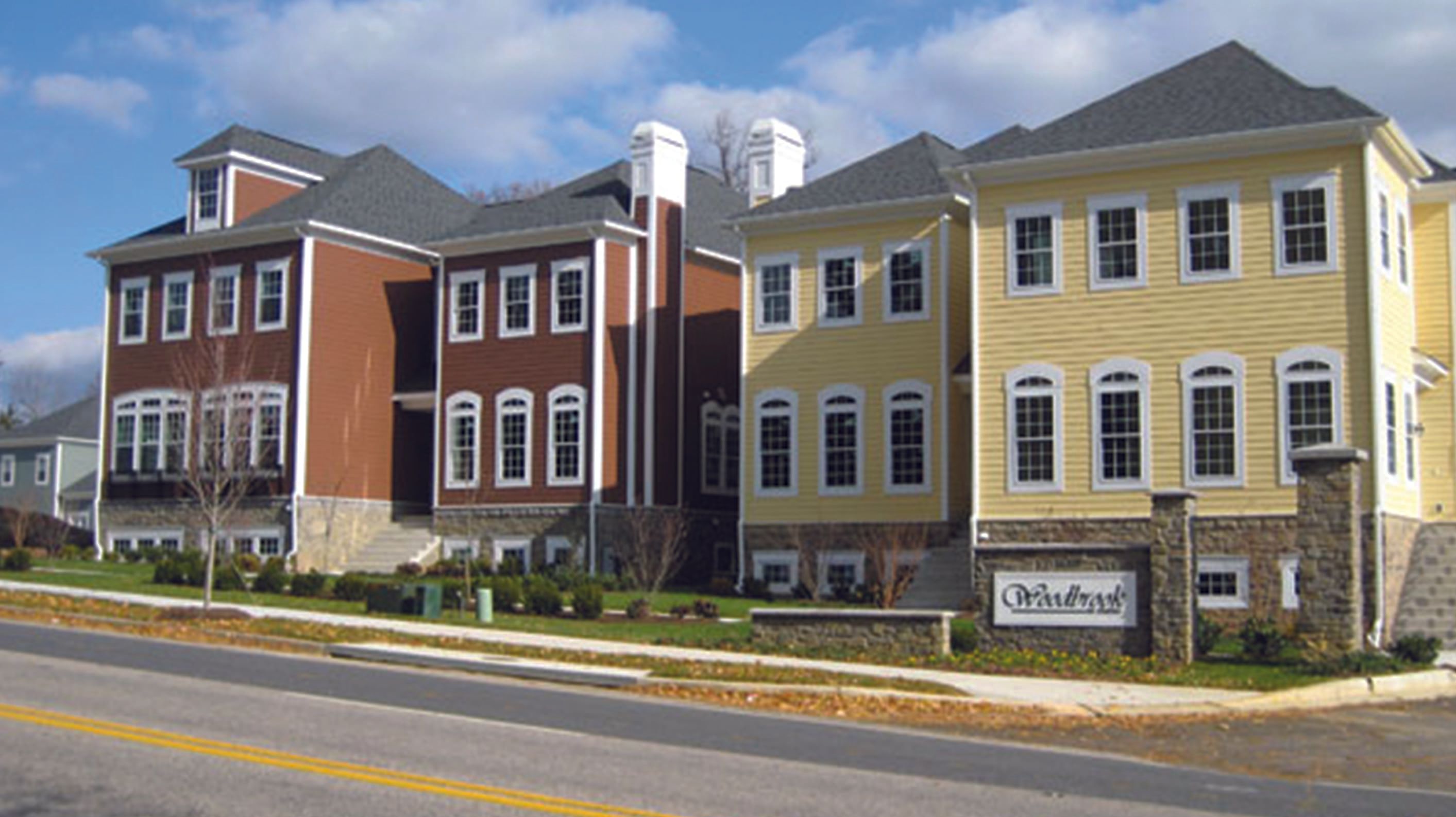 Two multi-story buildings with different colors and styles, situated next to a road.