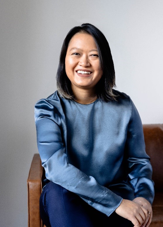 Xiyao Yang sits smiling on a sofa, wearing a blue top with a relaxed backdrop.