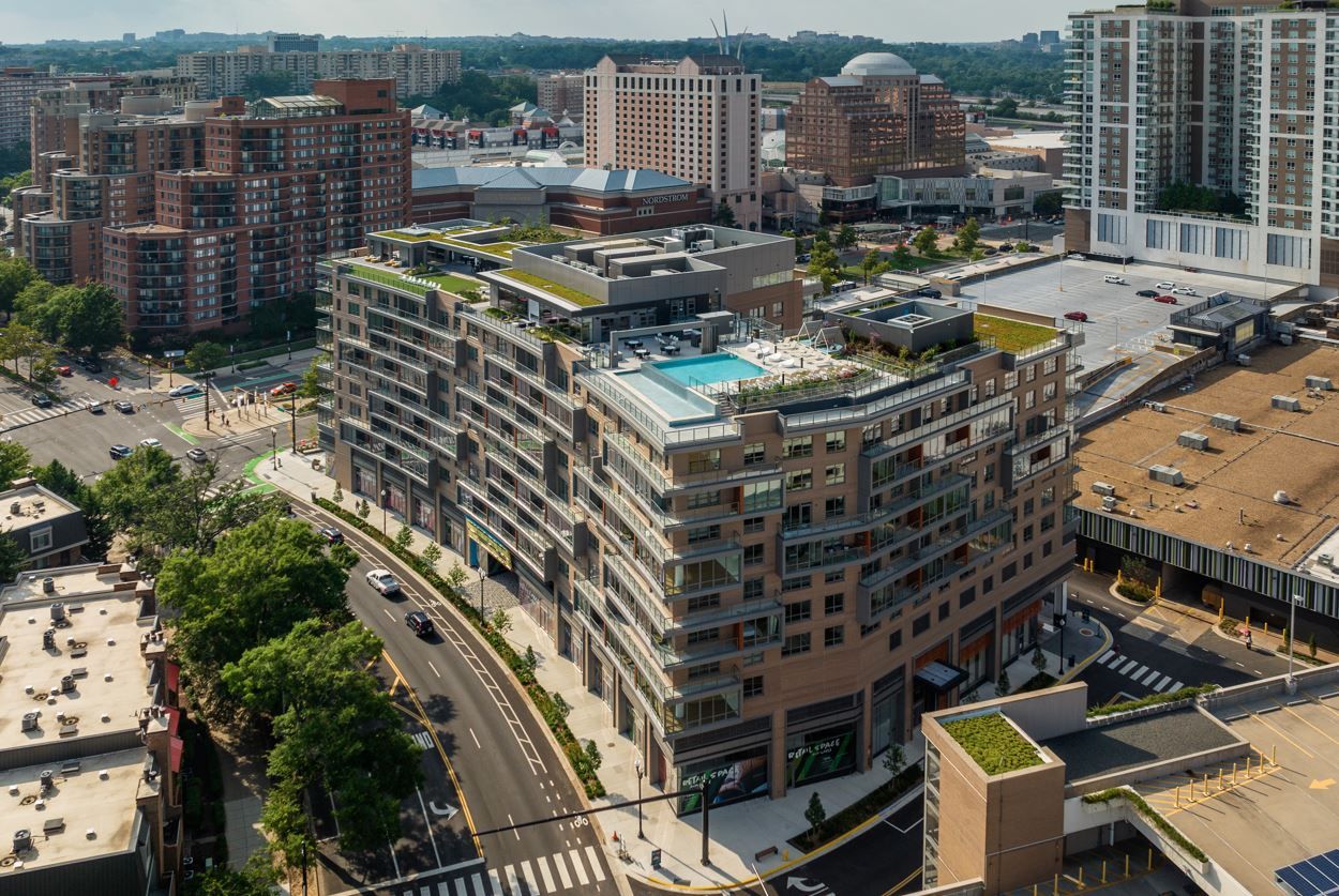 A modern building with a rooftop pool, surrounded by city streets and other structures.