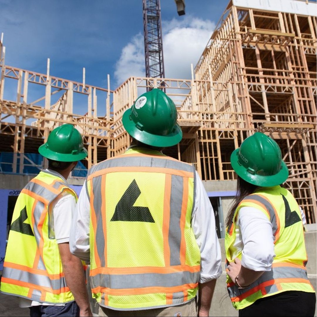 Three construction workers in hard hats observe a building site.