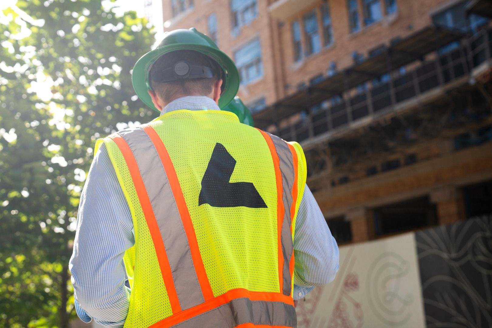A construction worker in a high-visibility vest seen from behind, outdoors.