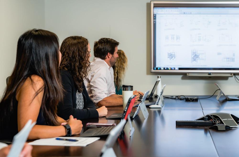 A group of people seated in a conference room, focused on a presentation screen.