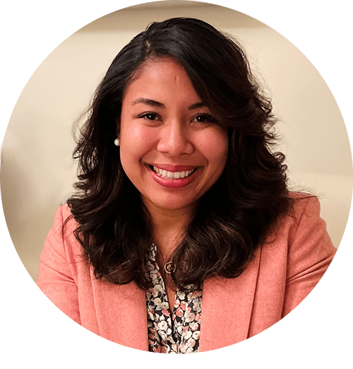 Smiling woman with curly hair wearing a pink blazer and floral shirt.
