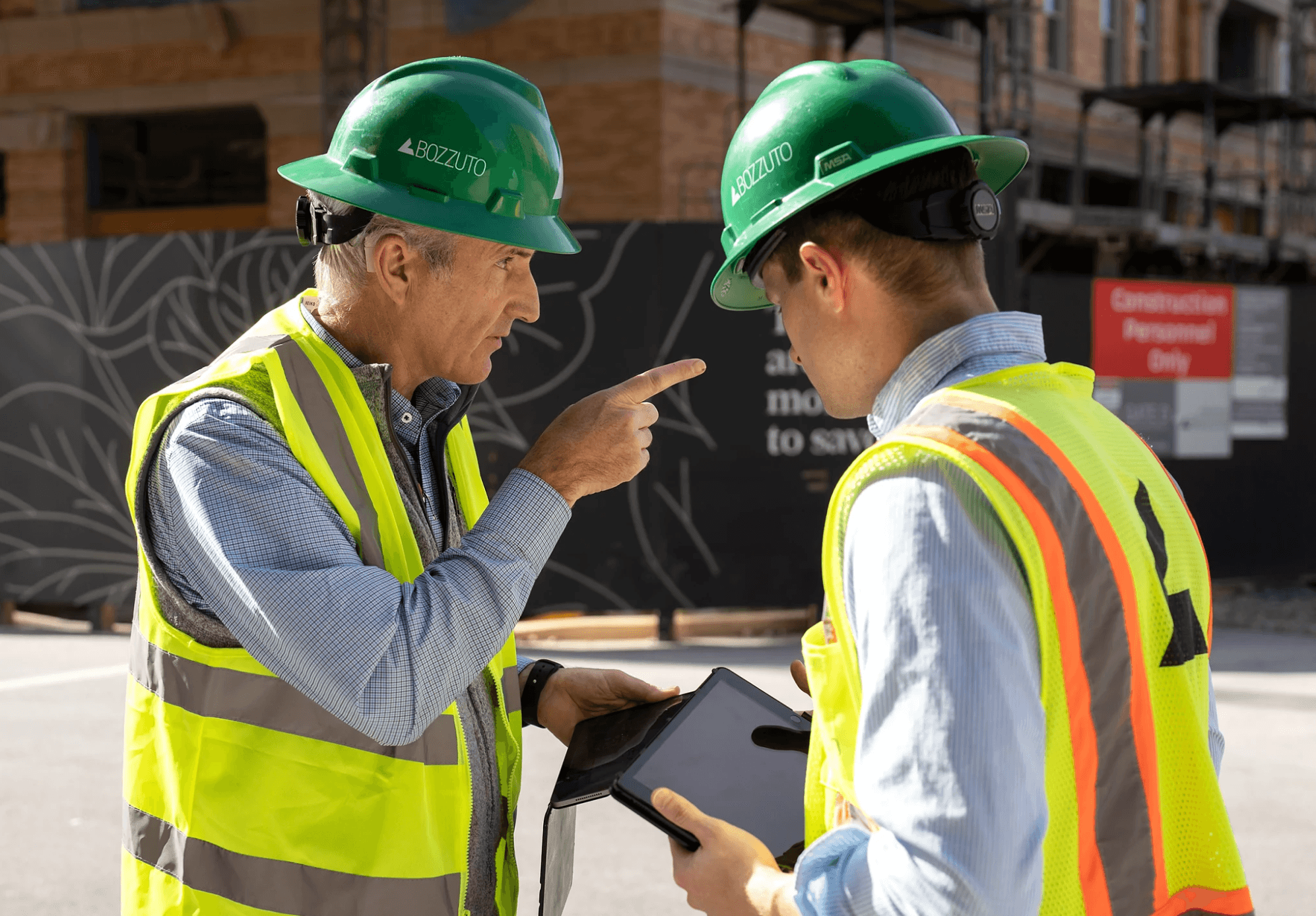 Two construction workers in safety gear discussing plans at a building site.
