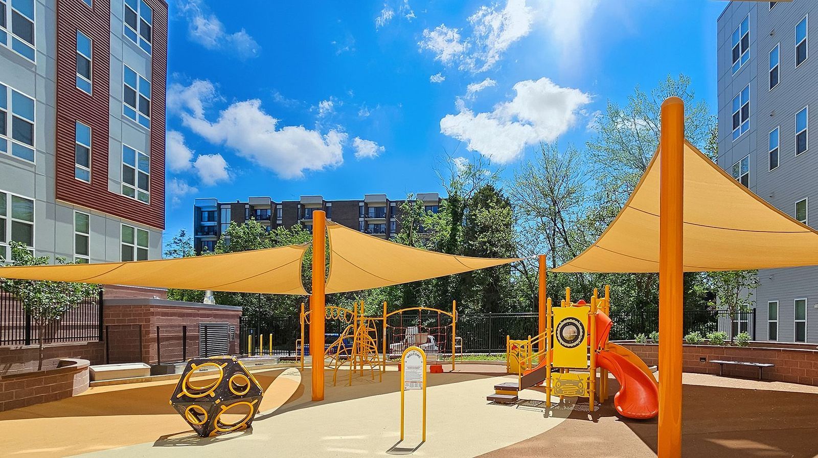 Children's playground with colorful equipment under shade awnings and a blue sky.