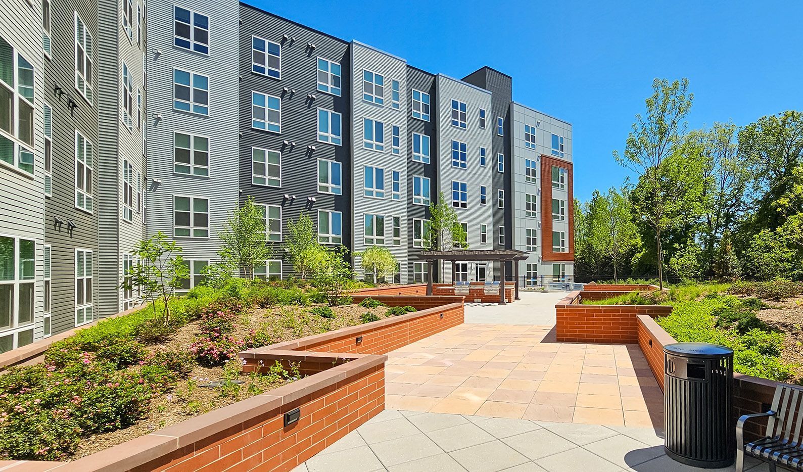 Modern apartment building with landscaped walkway and seating area.