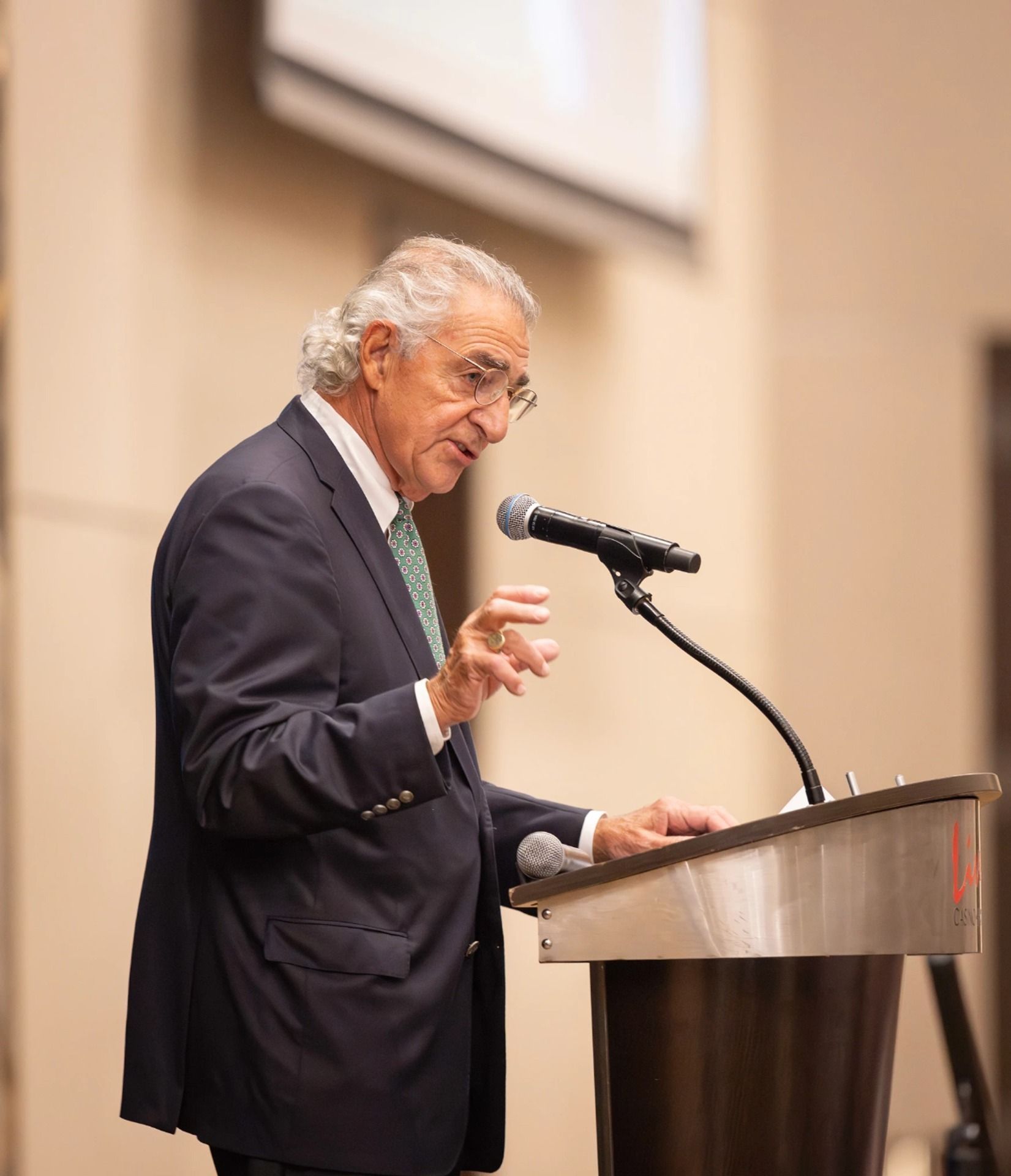 A speaker gestures while addressing an audience at a podium.