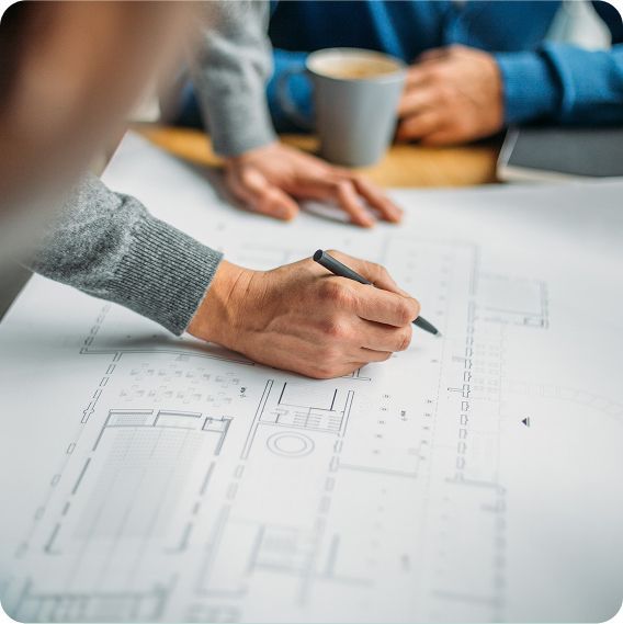 Hands reviewing architectural plans with a coffee cup nearby.