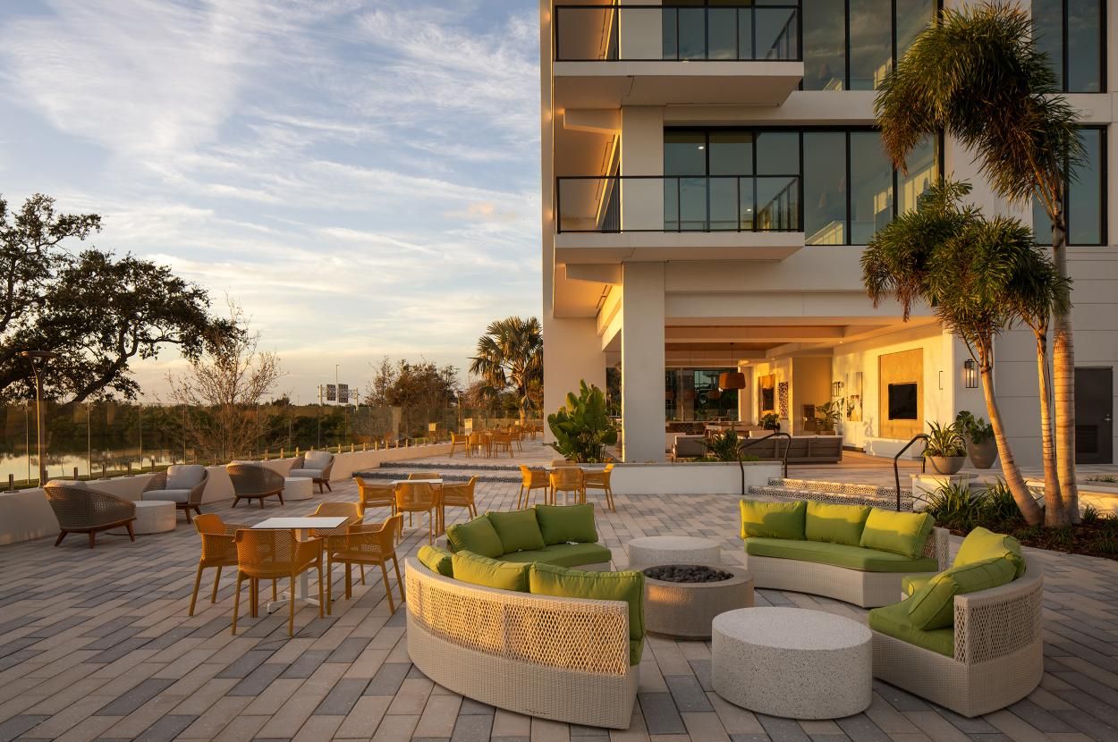 Modern outdoor seating area with green cushions, surrounded by a contemporary building and trees.
