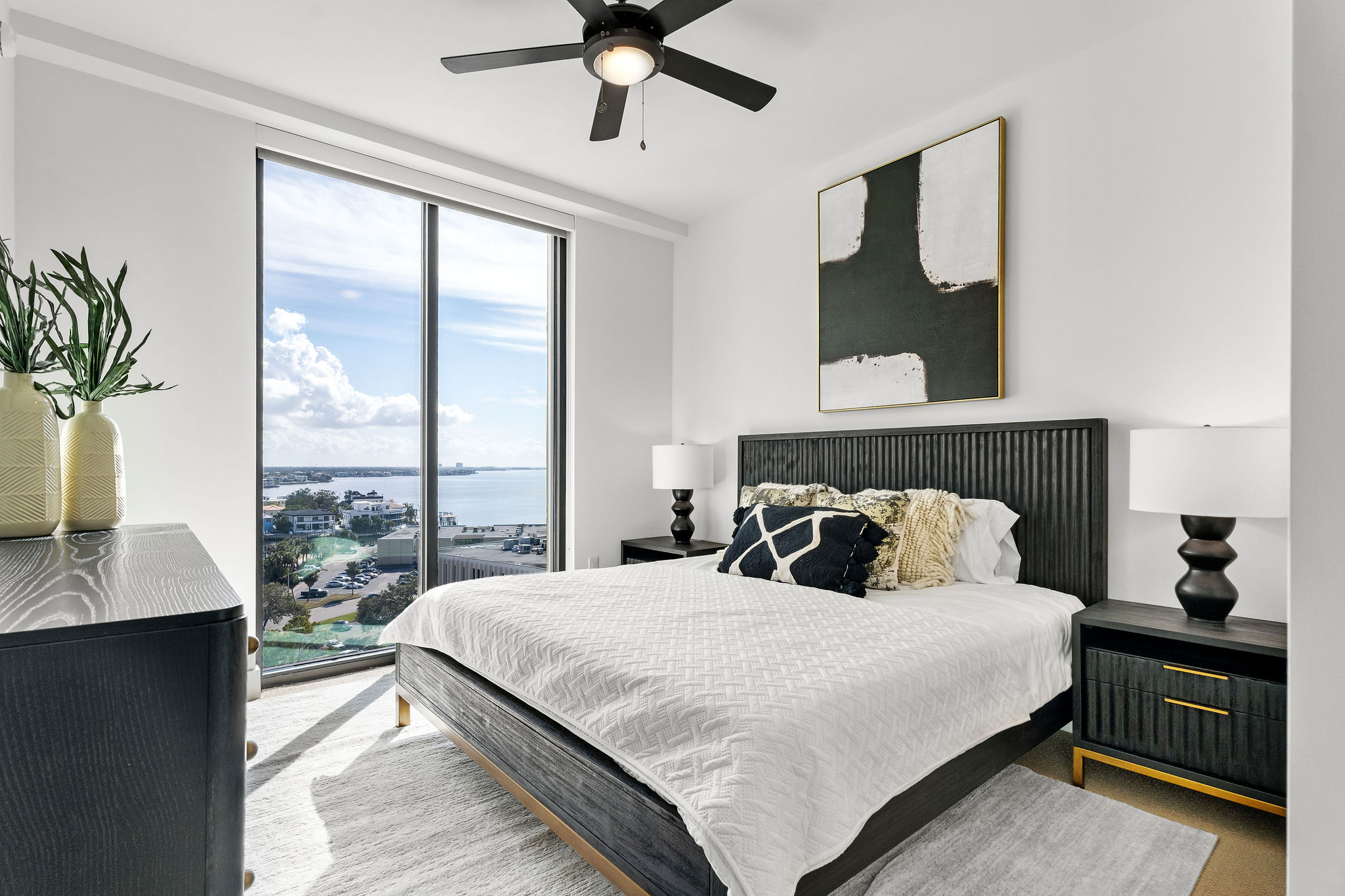 Modern bedroom with large windows, a bed, and minimalist decor overlooking a scenic view.