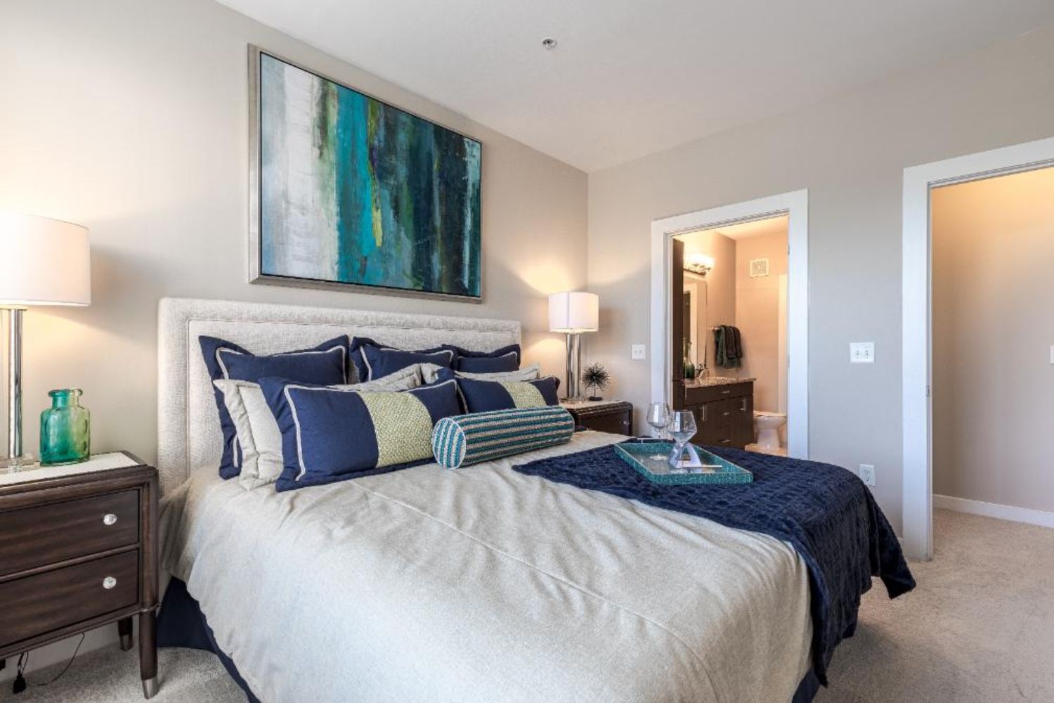 Photo of bedroom showing a bed filled with throw pillows and artwork above the headboard