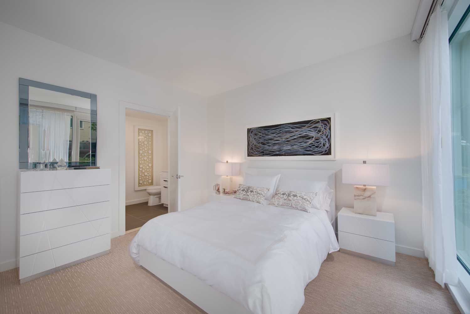 Bright, modern bedroom with white decor, a bed, nightstands, and a mirror.