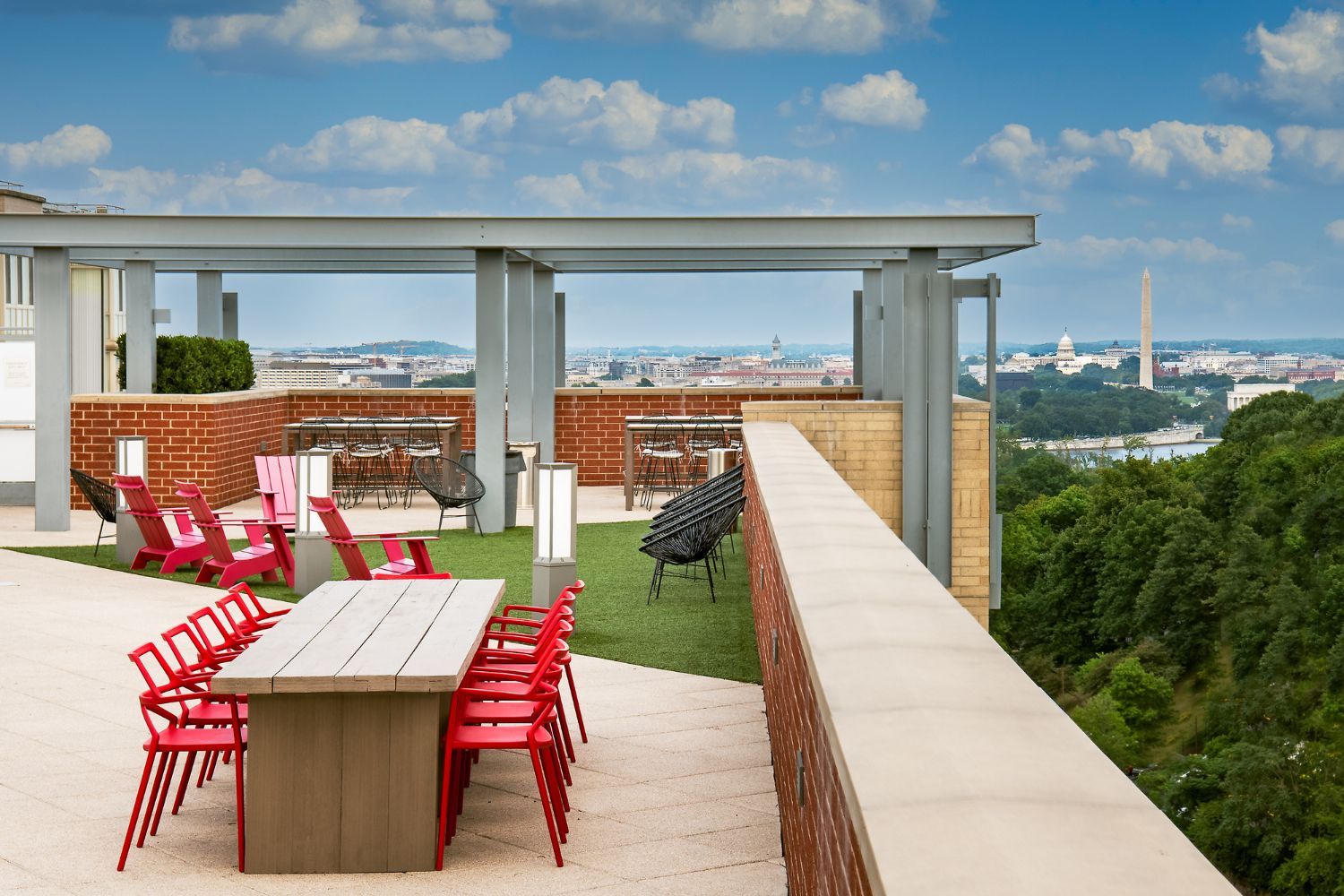 Rooftop patio with red chairs and a table overlooking a cityscape.