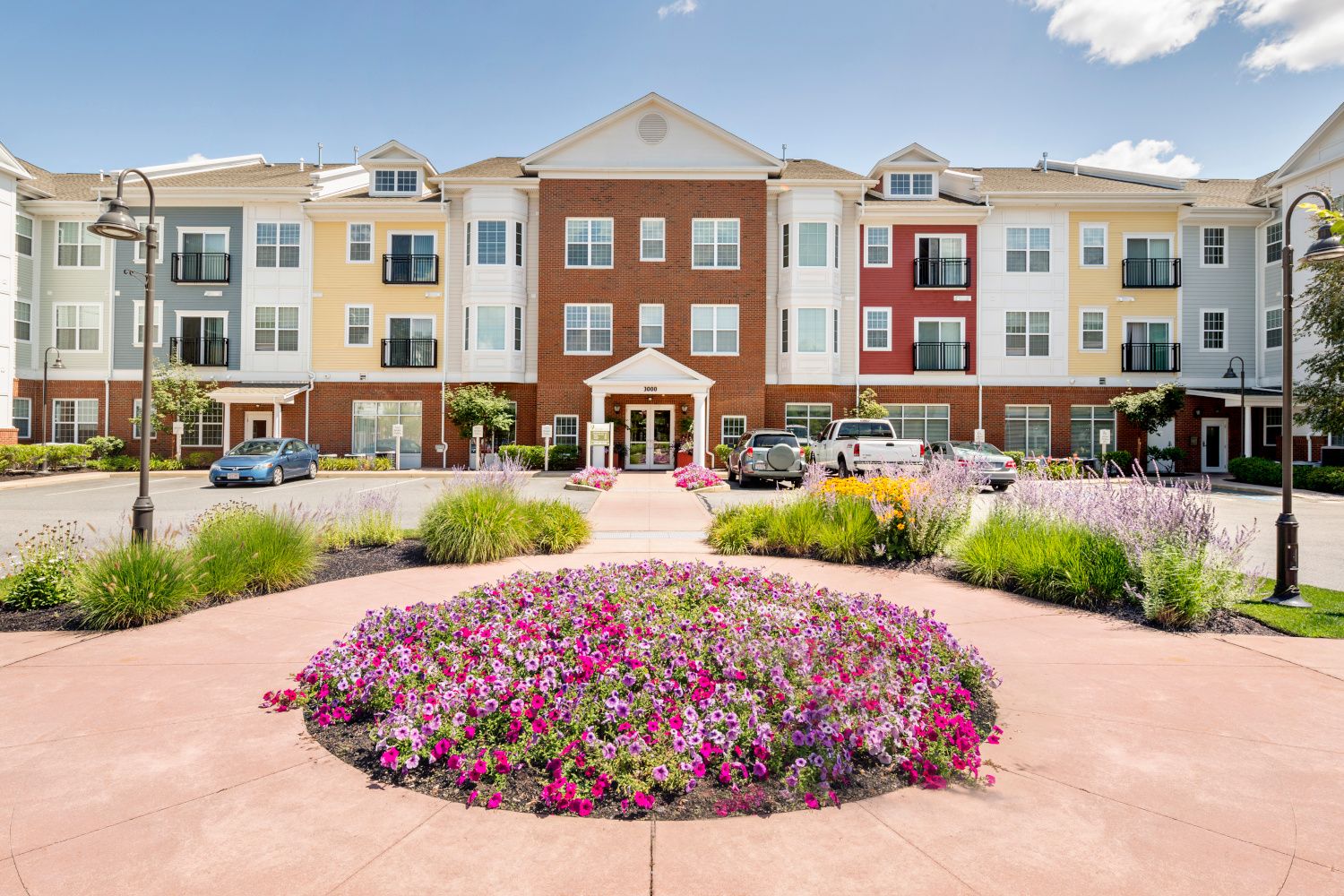 Multicolored apartment building with flower garden and parked cars in front.