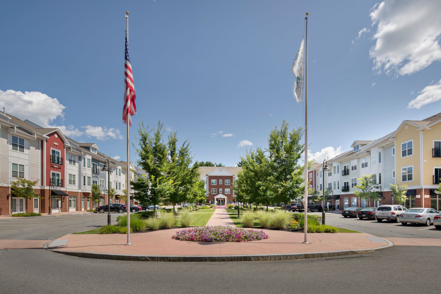 A landscaped plaza with residential buildings and flags under a blue sky.