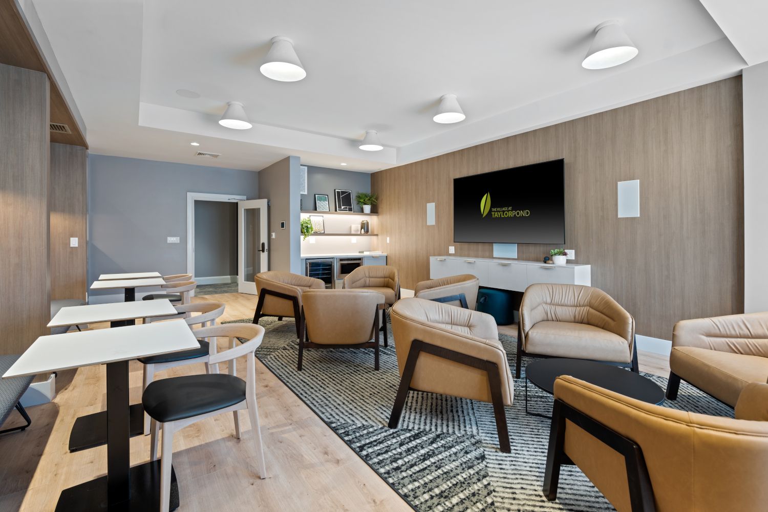Modern lounge area with beige chairs, tables, and a wall-mounted TV.