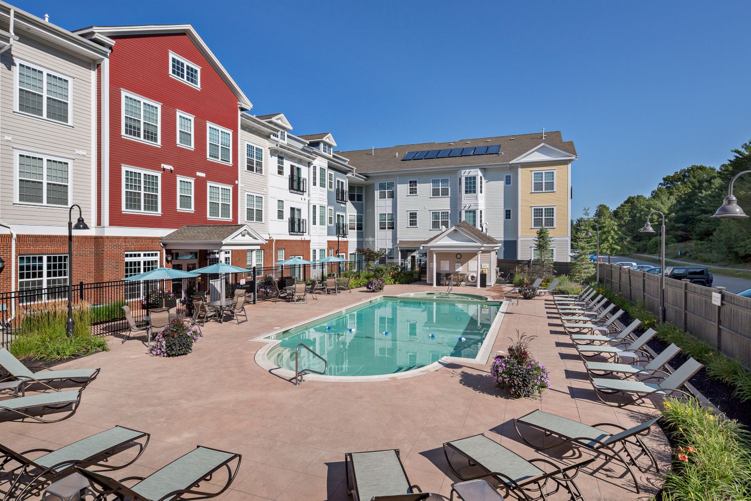 Swimming pool surrounded by lounge chairs and apartment buildings under a clear blue sky.