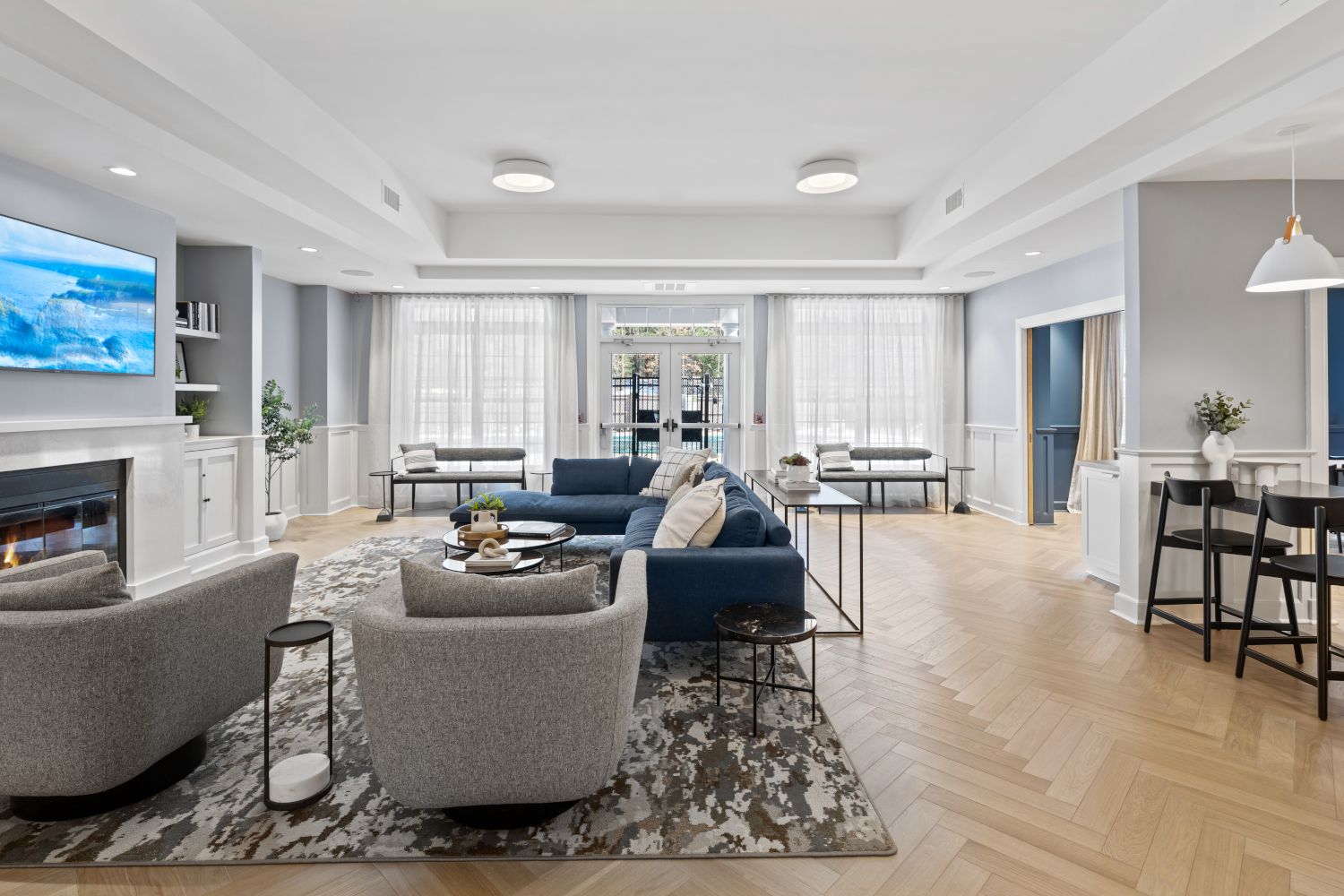 Modern living room with blue sofa, gray armchairs, and a television on the wall.