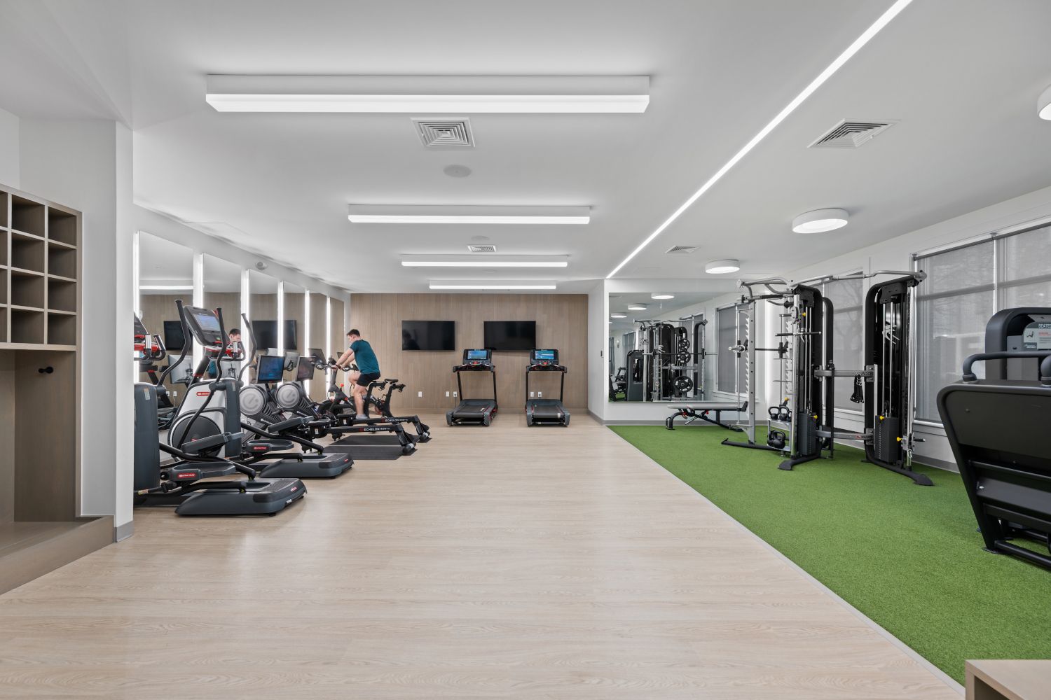Modern gym with exercise equipment, green turf, and well-lit space.