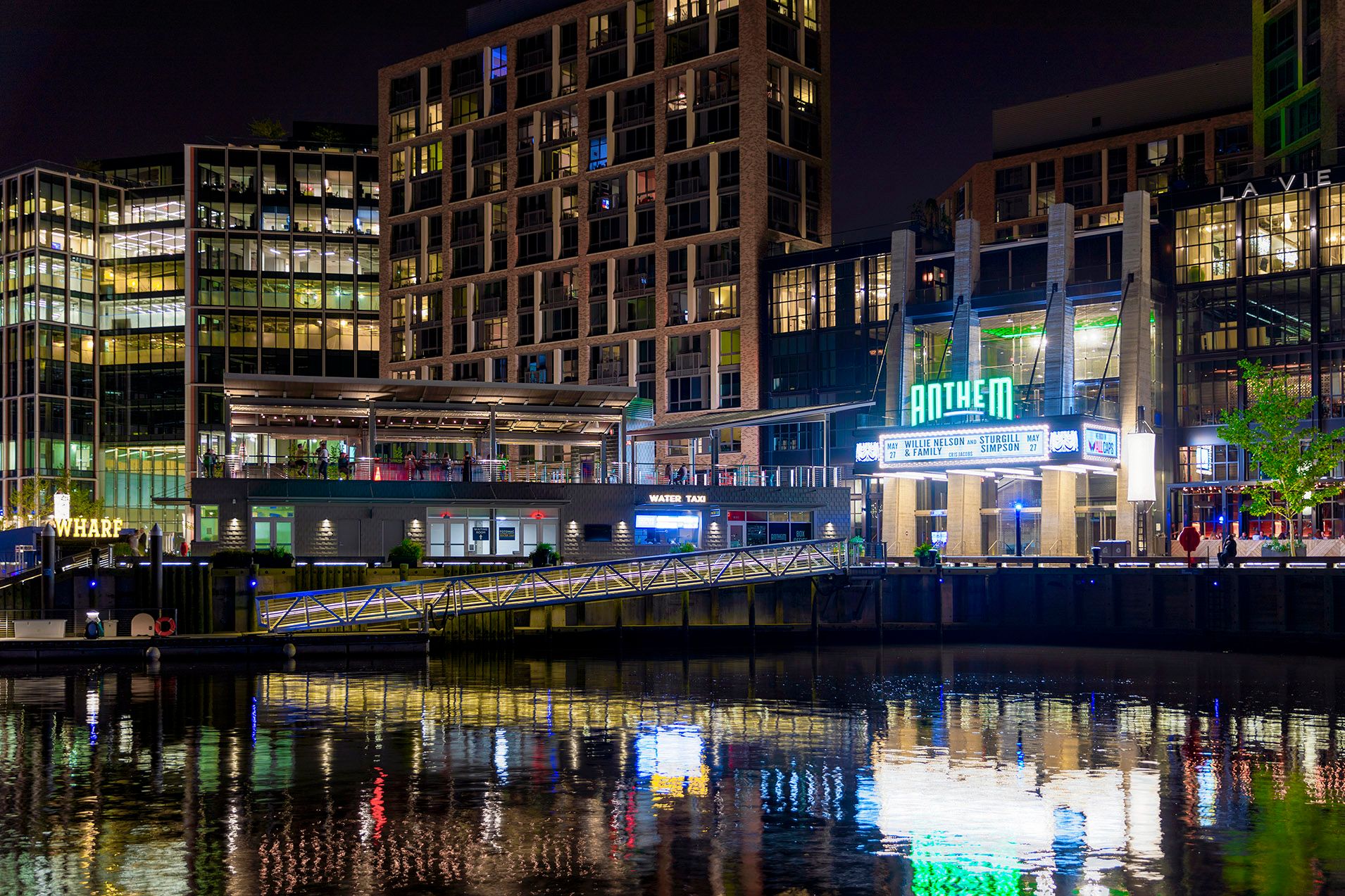 City skyline at night with buildings reflecting on water.