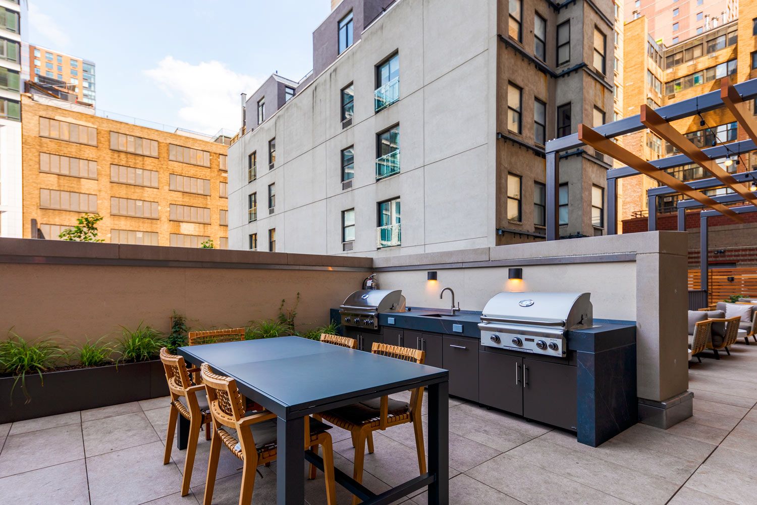 Rooftop patio with a dining table, grills, and urban buildings in the background.