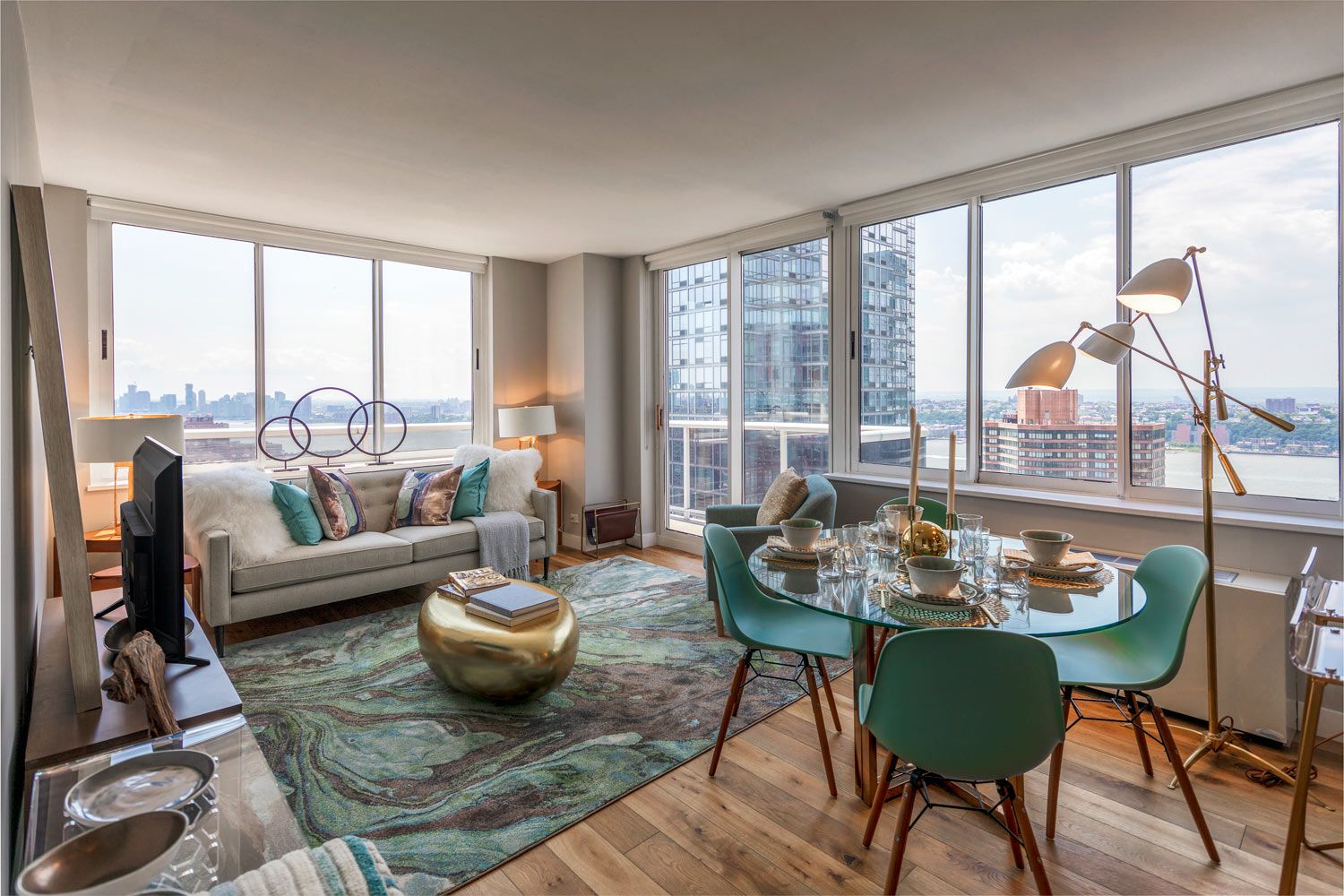 Modern living room with large windows, a sofa, dining table, and city views.