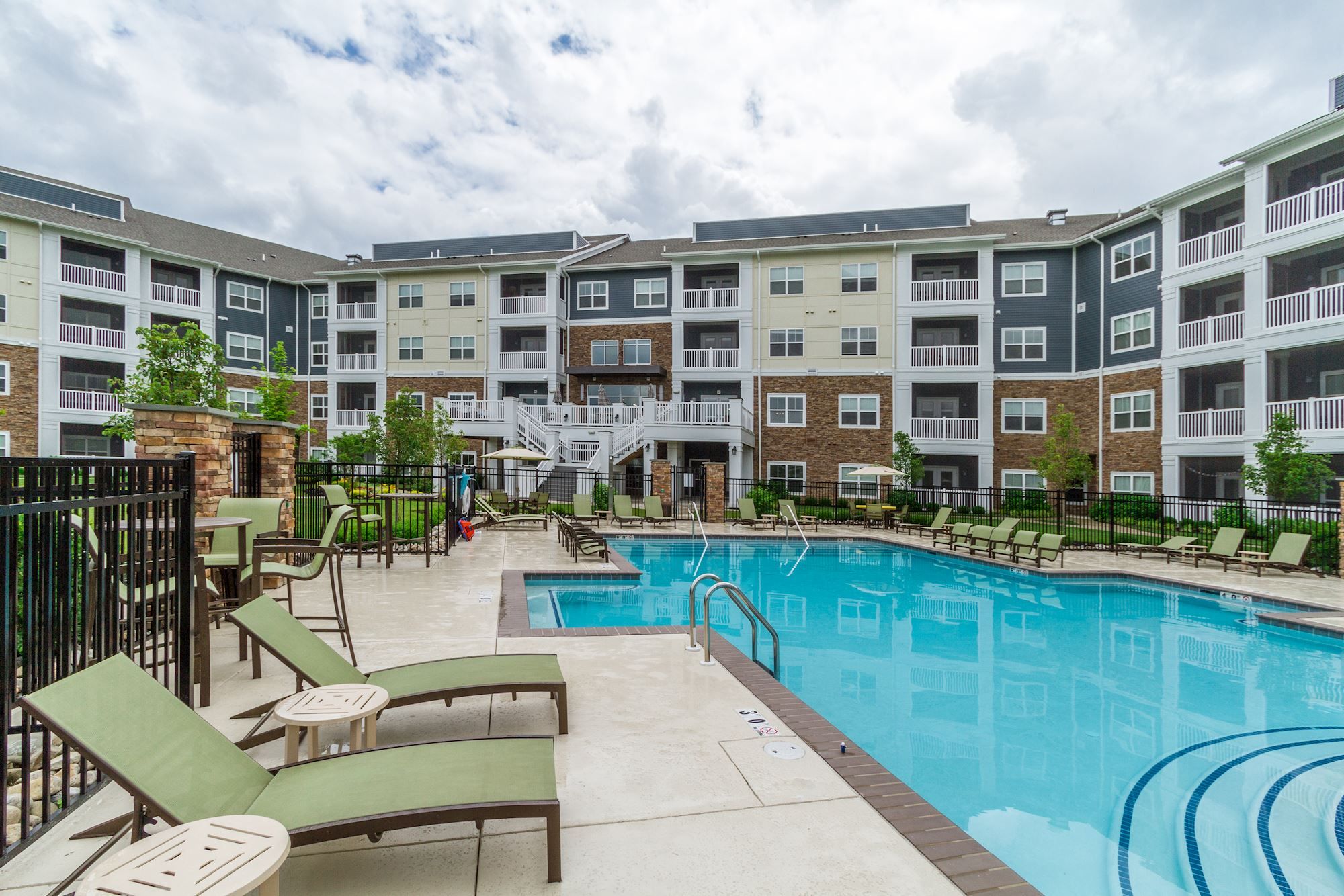 Apartment complex with a pool surrounded by lounge chairs and cloudy skies.