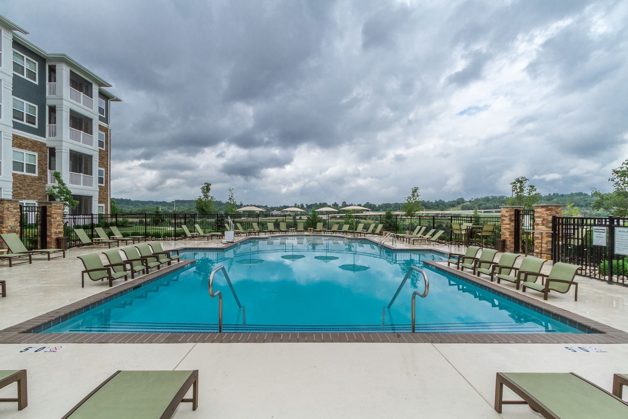 A swimming pool surrounded by lounge chairs, with cloudy skies in the background.