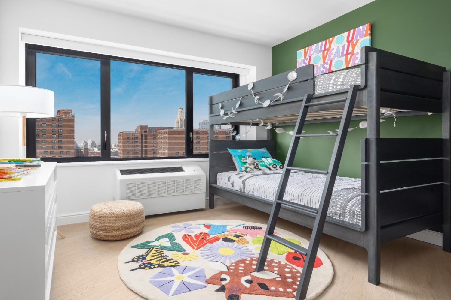 A modern bedroom with a bunk bed, colorful rug, and large window showing a city view.
