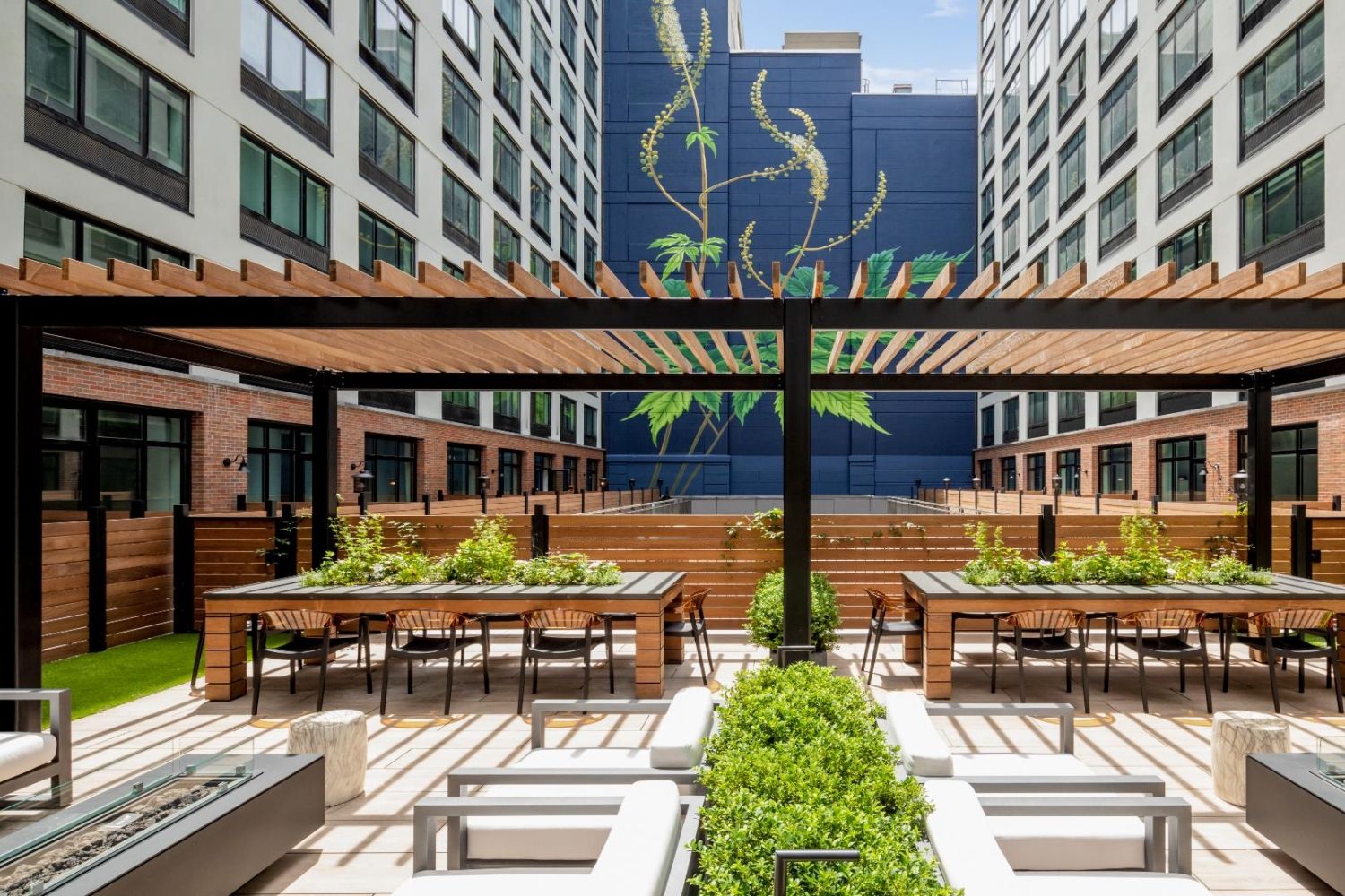 Modern courtyard with greenery, seating areas, and a mural on the building in the background.