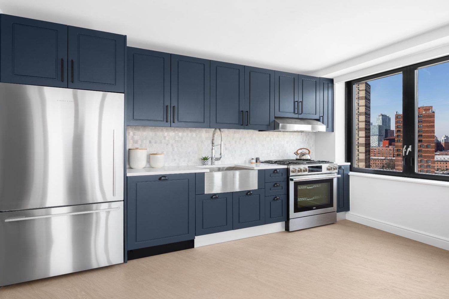 Modern kitchen with navy cabinets, stainless steel appliances, and large window.