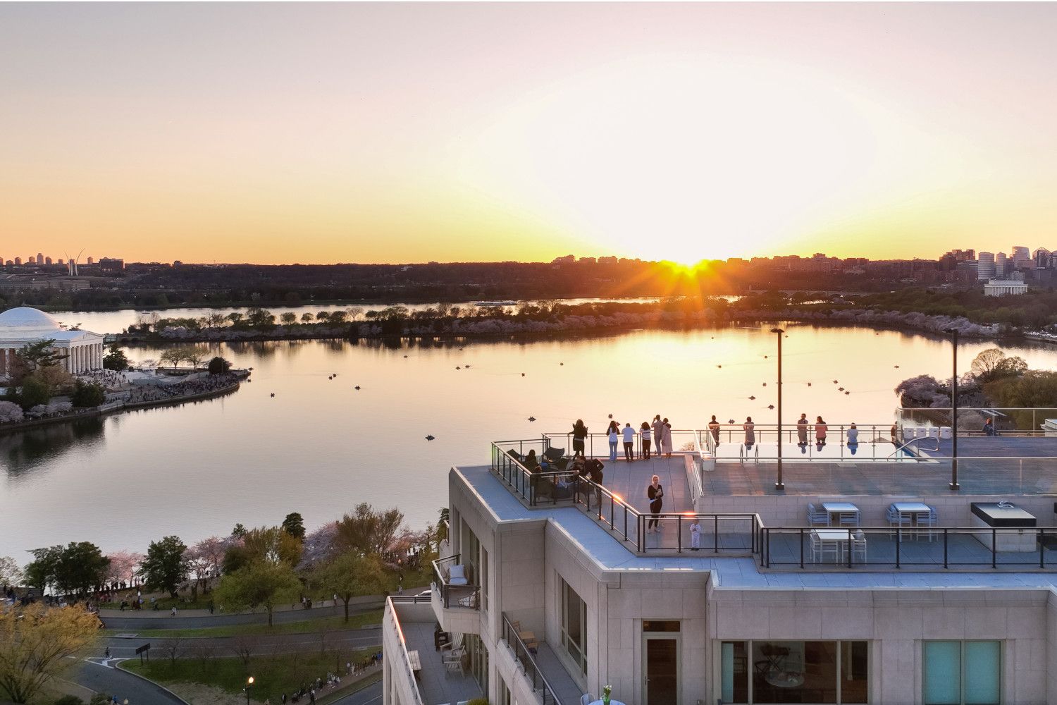 Sunset over a calm lake, with people silhouetted on a rooftop.
