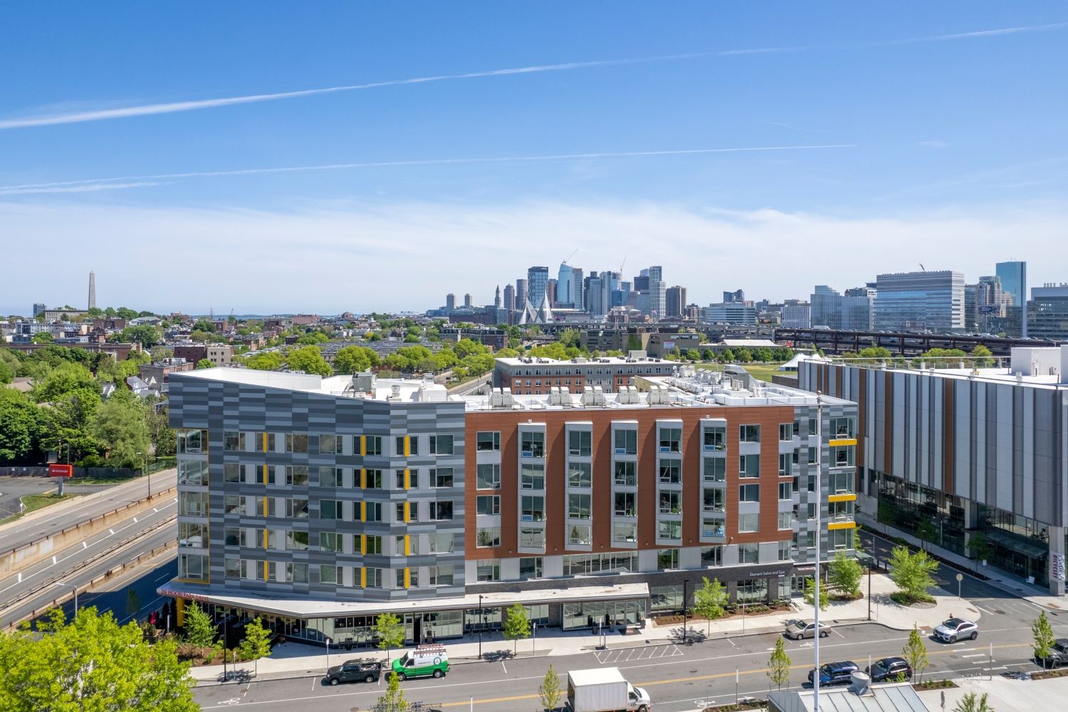 Modern multi-story building with city skyline in the background and clear blue sky.