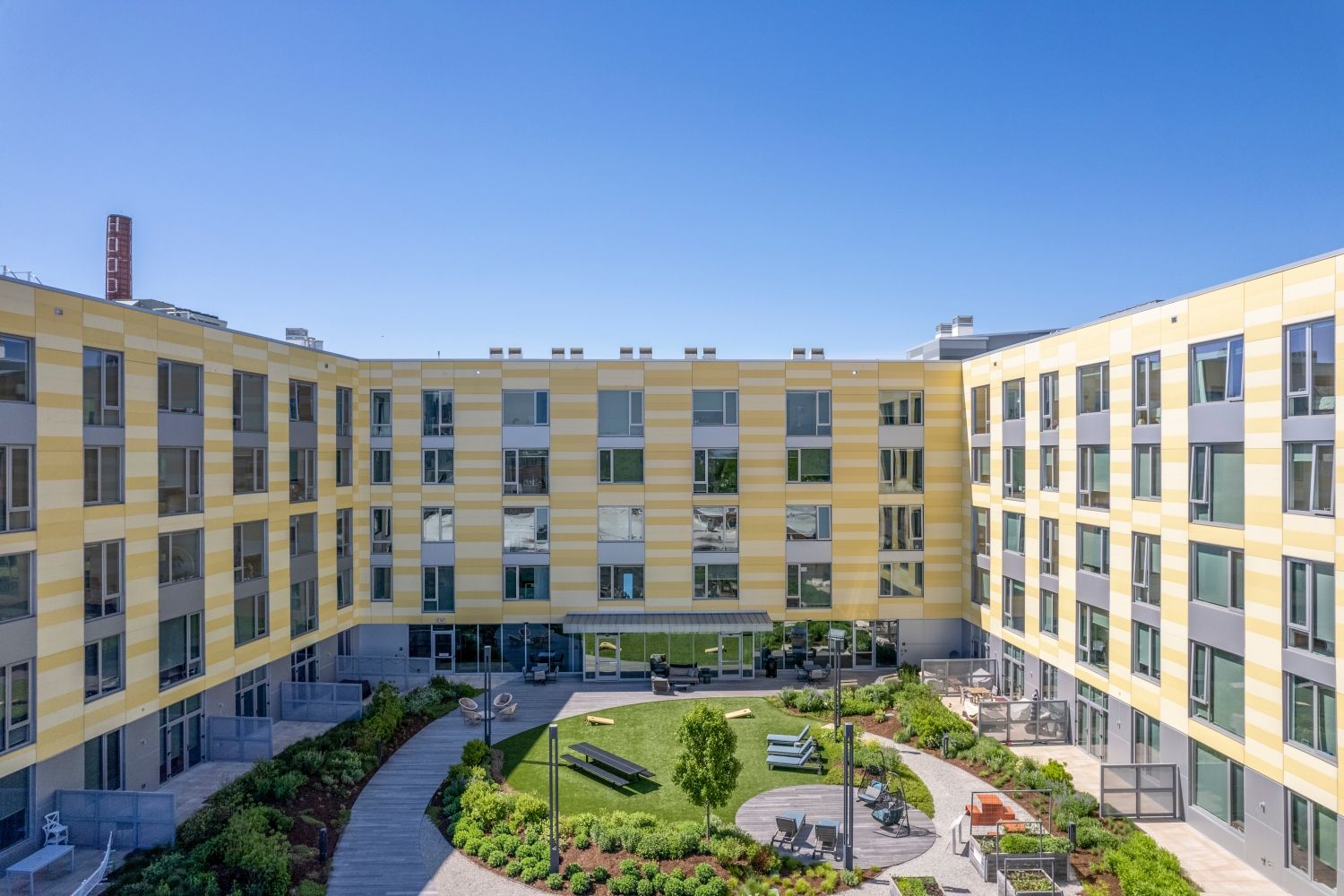 Modern building with a courtyard, green spaces, and clear blue sky.
