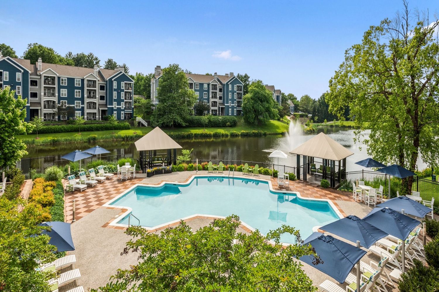 View of a poolside area with lounge chairs by a lake and apartment buildings in the background.