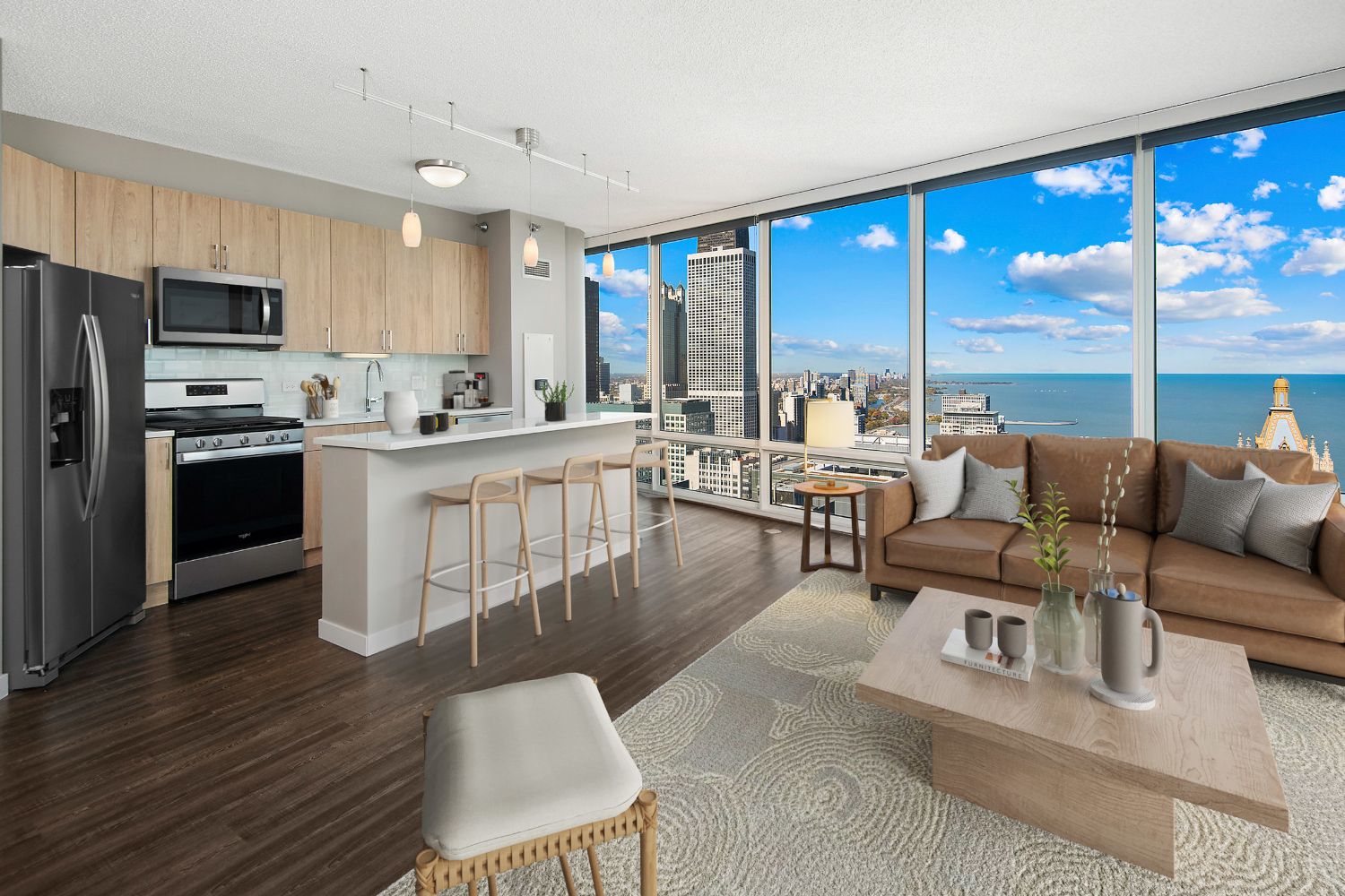 Wide angle of a furnished kitchen and living area, with large windows in the background.