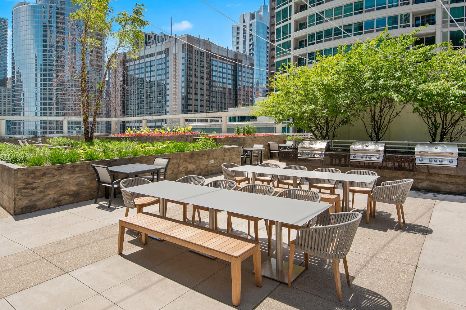 Wide angle of Atwater's sundeck, private outdoor grill area, and patio furniture with foliage and the cityscape in the background.