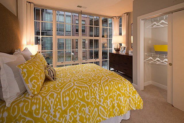 Cozy bedroom with a yellow patterned bedspread and large windows.
