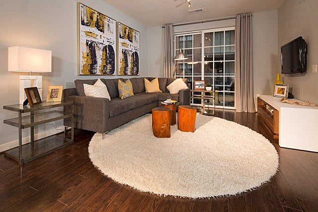 A modern living room with a gray sofa, two orange tables, and a large round rug.