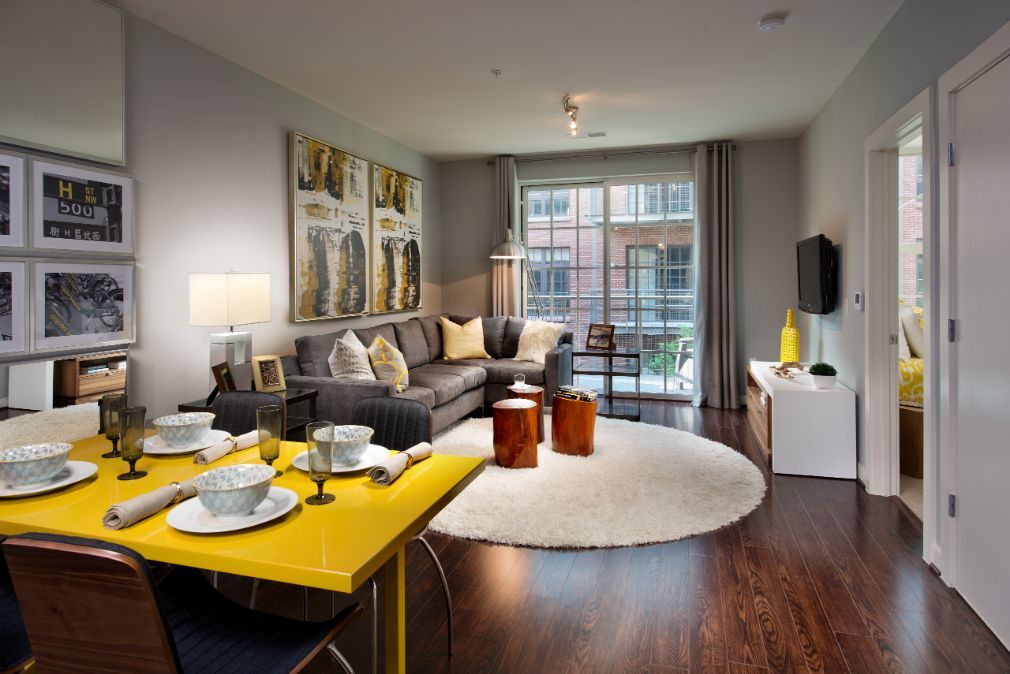 Modern living room with a dining area, featuring a sofa, table, and large windows.