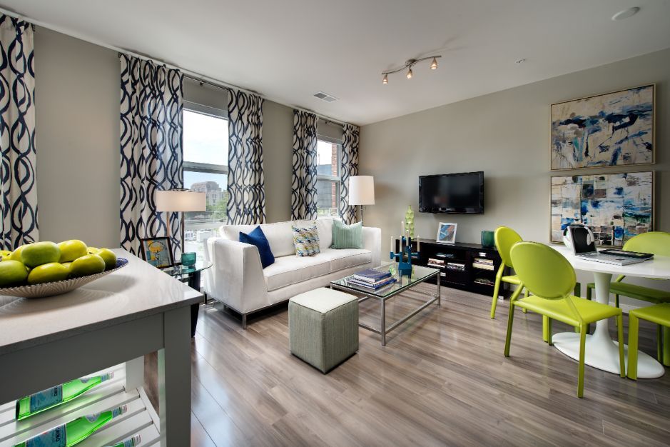 Modern living room with light furniture, green accents, and a dining area.