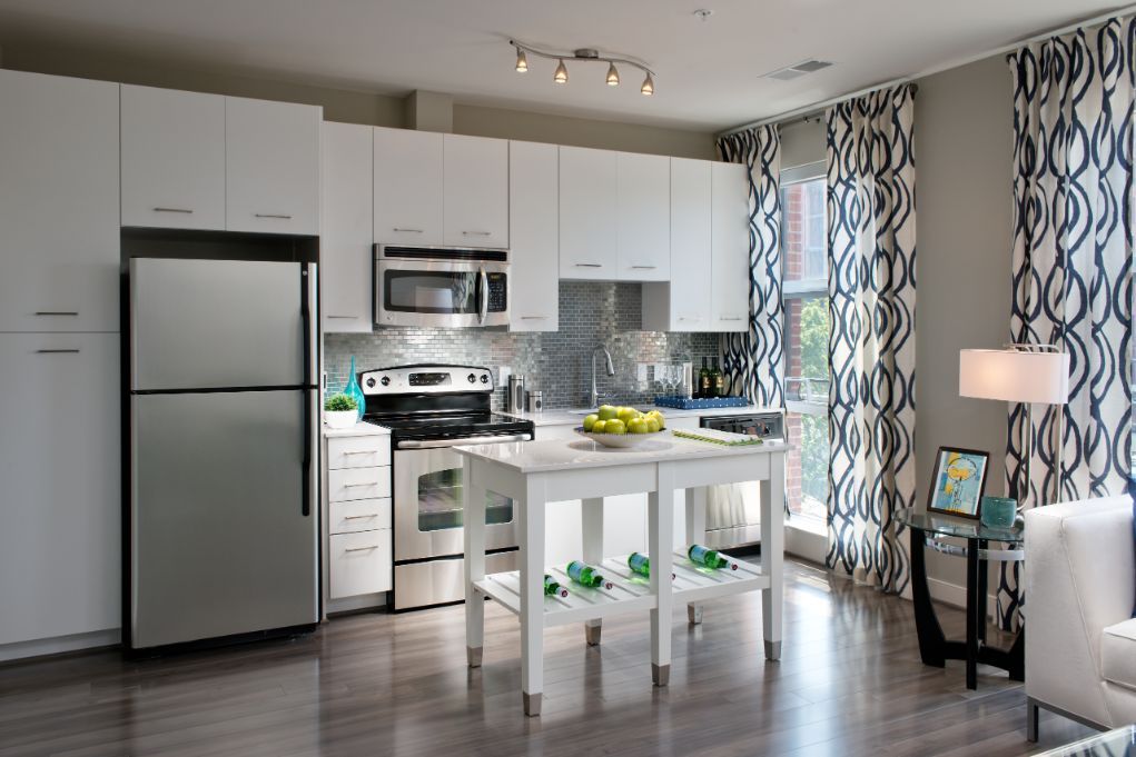 Modern kitchen with white cabinetry, stainless steel appliances, and large windows with curtains.