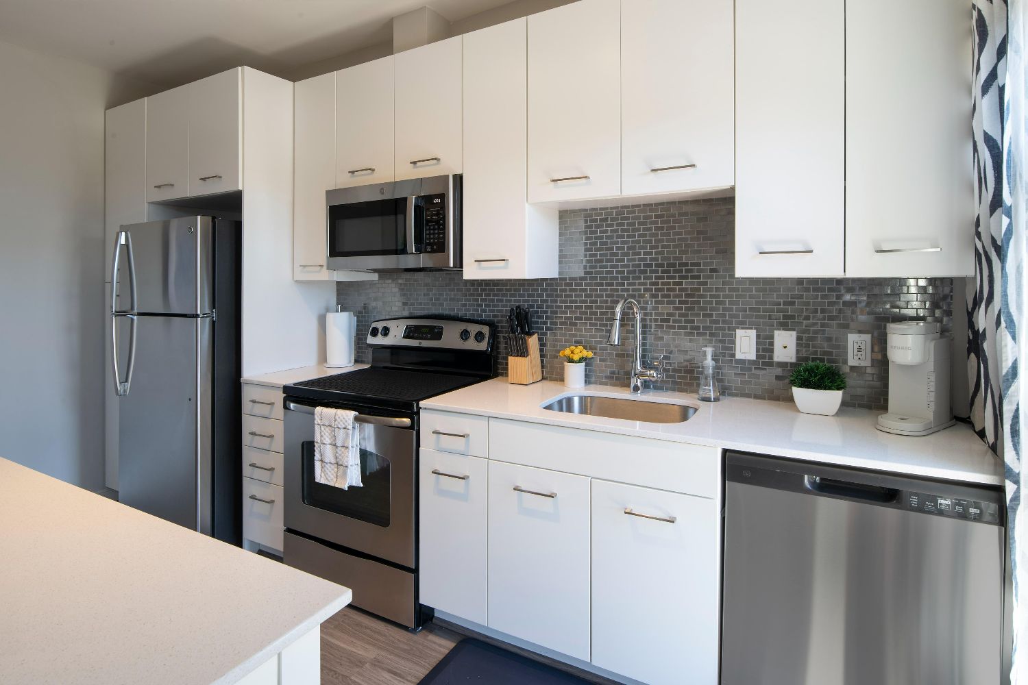 Kitchen detail at 77 H with white cabinets, stainless steel refrigerator, range, microwave, dishwasher, sink, and gray tile
