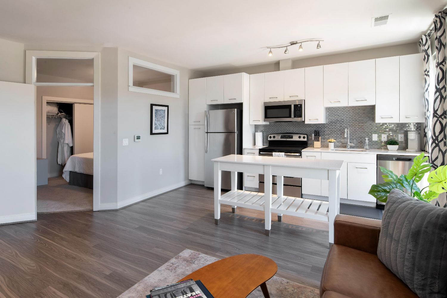 Apartment kitchen at 77 H with white cabinets, stainless steel appliances, island, bedroom entry, and wood-style flooring