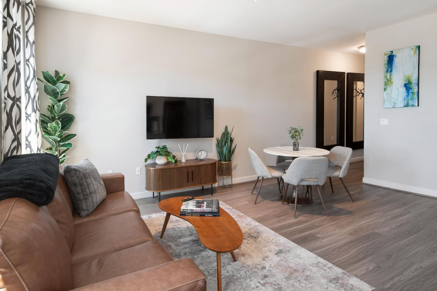Apartment living and dining area at 77 H with sofa, TV, round dining table, plants, and wood-style flooring