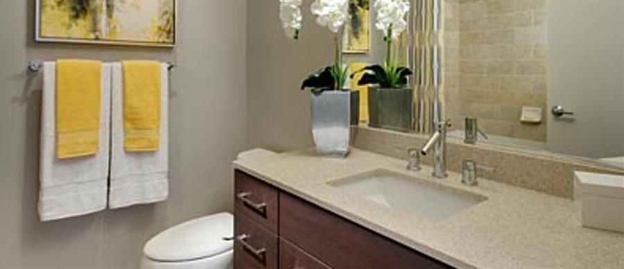 Modern bathroom with a sink, mirror, toilet, and yellow towels on display.