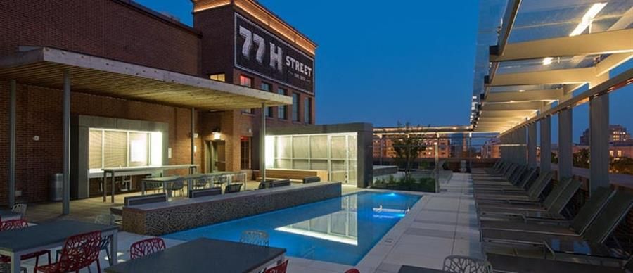 Modern rooftop pool area with lounge chairs and city skyline at dusk.