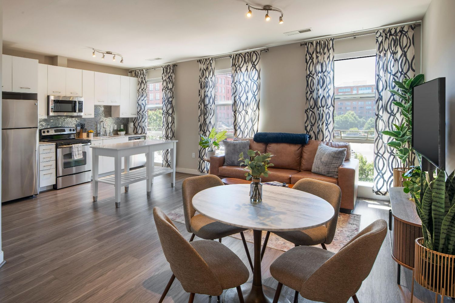 Apartment at 77 H with kitchen, dining table, leather sofa, TV, patterned curtains, and large windows