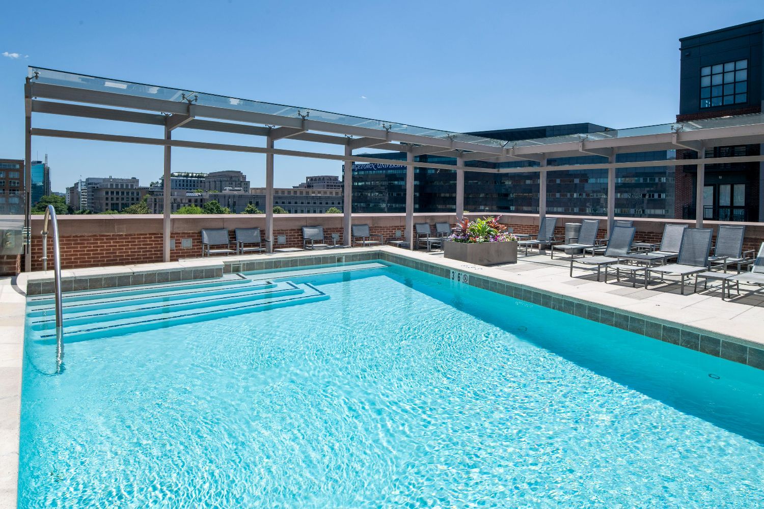 Rooftop pool at 77 H with blue water, lounge chairs, glass railing, pergola, and city view